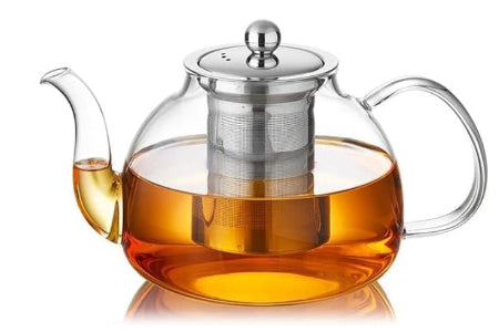 Glass teapot with a metal lid and handle, filled with tea, on a white background